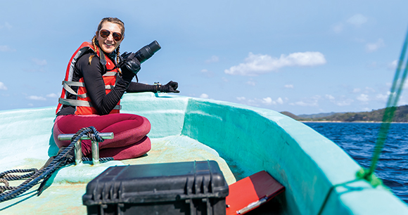 Happy marine biologist working while taking photo sitting at the edge of a boat