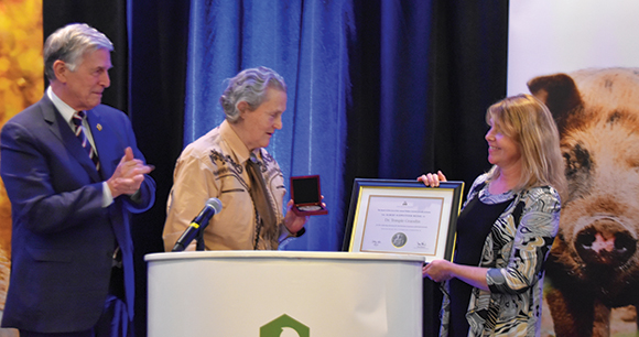 Susan Milward awards Dr. Temple Grandin on stage with plaque