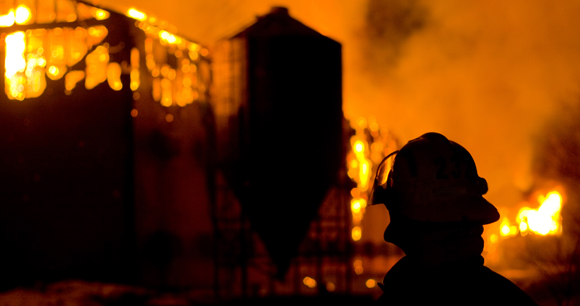 silhouette of firefighter in front of burning farm