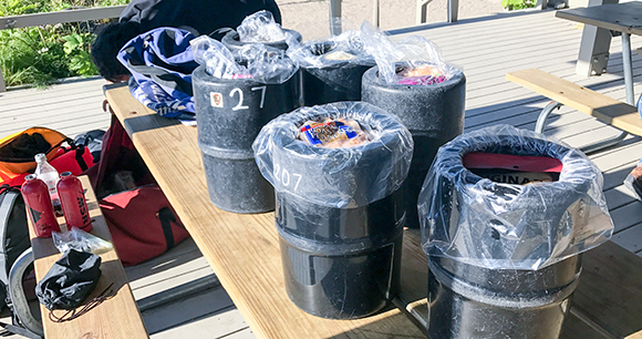 Six bear canisters are displayed on an picnic table