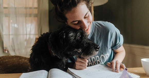 woman cuddling dog while writing at table
