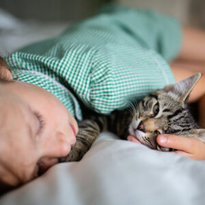 A child in a green shirt lying on a bed while holding a tabby cat.