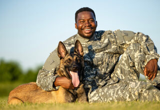 smiling soldier hugging canine armed forces member with tongue out